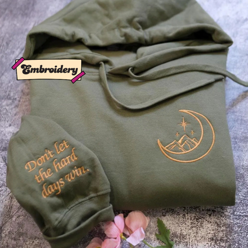 A green hoodie with an embroidered design and text on the front, along with a small pink flower on the side.